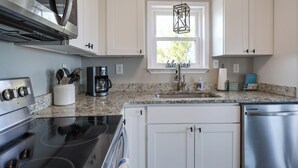 A modern kitchen with white cabinets, stainless steel appliances, a granite countertop, and a window with a hanging light fixture. - Beach “N” Bay Getaway Sleeps 9. Enjoy Beach Time,  Fishing, Kayaking. Steps Away (Gulf Shores)
