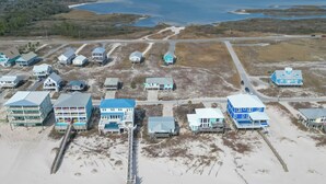 An aerial view of a coastal area with multiple beachfront properties, including houses and a pier extending into the water. - Beach “N” Bay Getaway Sleeps 9. Enjoy Beach Time,  Fishing, Kayaking. Steps Away (Gulf Shores)