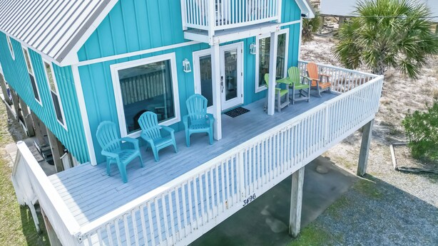 A turquoise two-story house with a balcony, featuring a white railing and several chairs. - Beach “N” Bay Getaway Sleeps 9. Enjoy Beach Time,  Fishing, Kayaking. Steps Away (Gulf Shores)