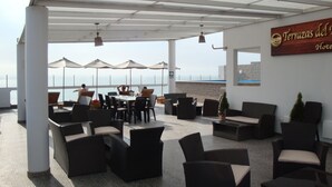 Un'area salotto esterna con tavoli, sedie e ombrelloni, affacciata sul mare.
