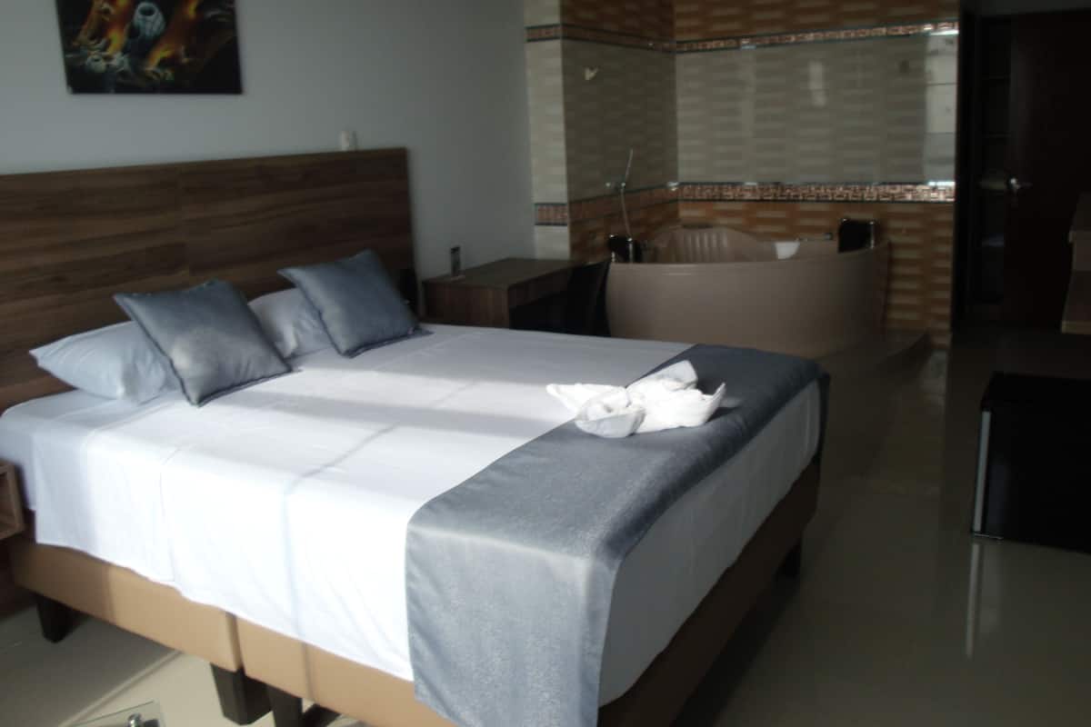 A hotel room with a bed, a nightstand, a bathroom with a bathtub, and a shower area.