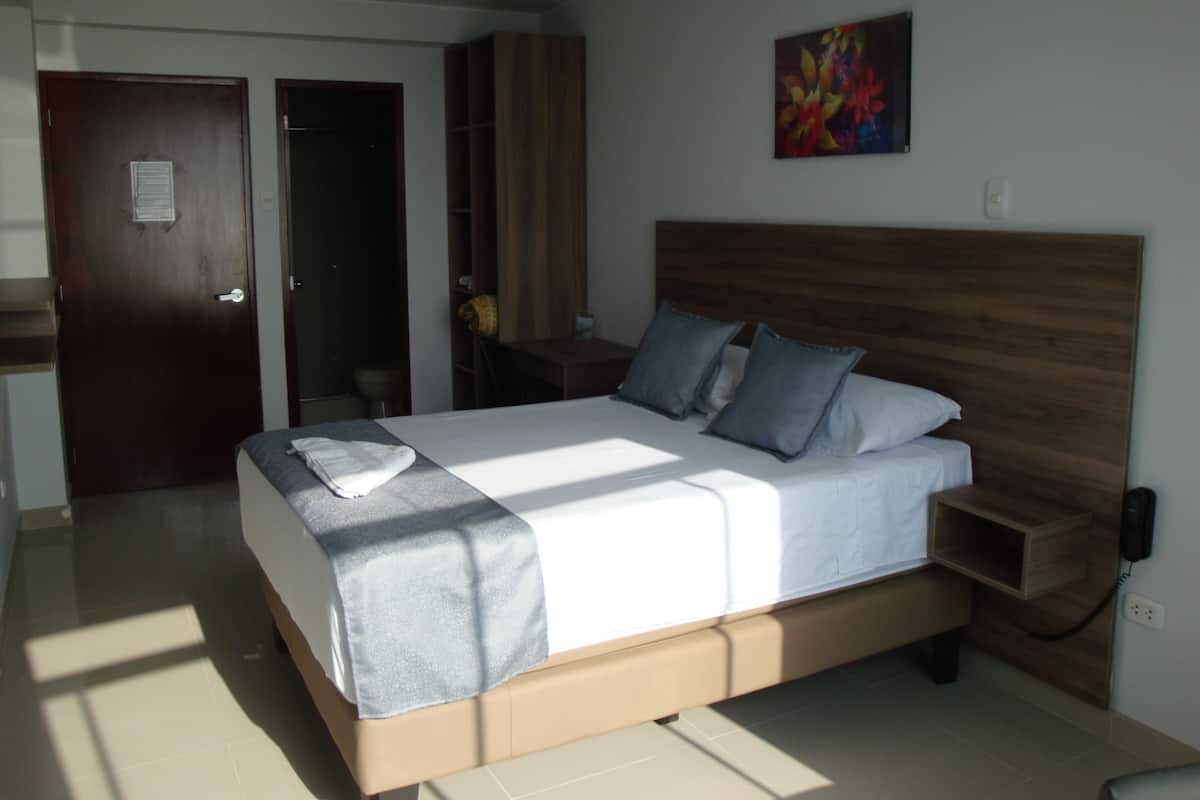 A neatly made bed with a wooden headboard, a bedside table with a phone, and a small wooden cabinet.