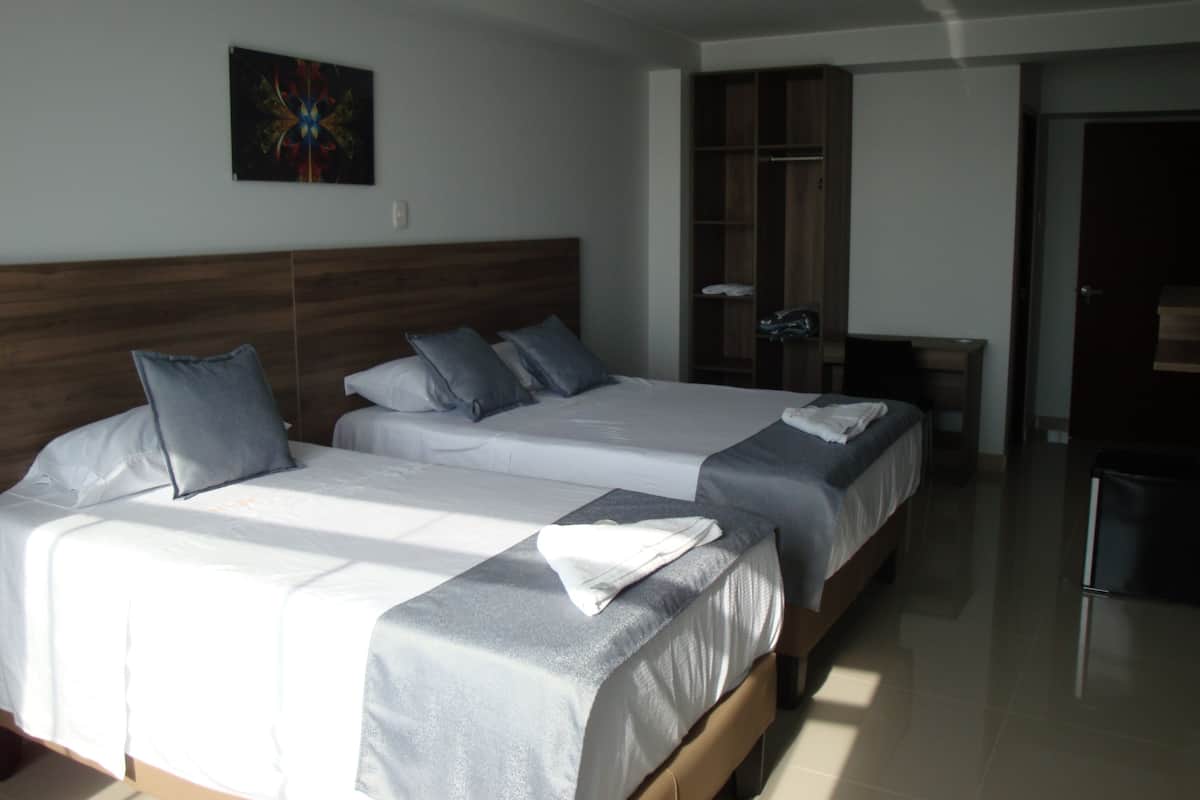 A hotel room with two beds, a wardrobe, and a desk.