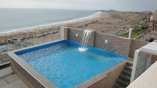 Una piscina sul tetto con cascata, affacciata su una spiaggia e l'oceano.