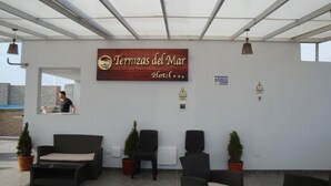 Un'area reception di un hotel con un cartello che indica "Terrazas del Mar Hotel". Sono presenti diverse sedie e piante in vaso disposte per gli ospiti.