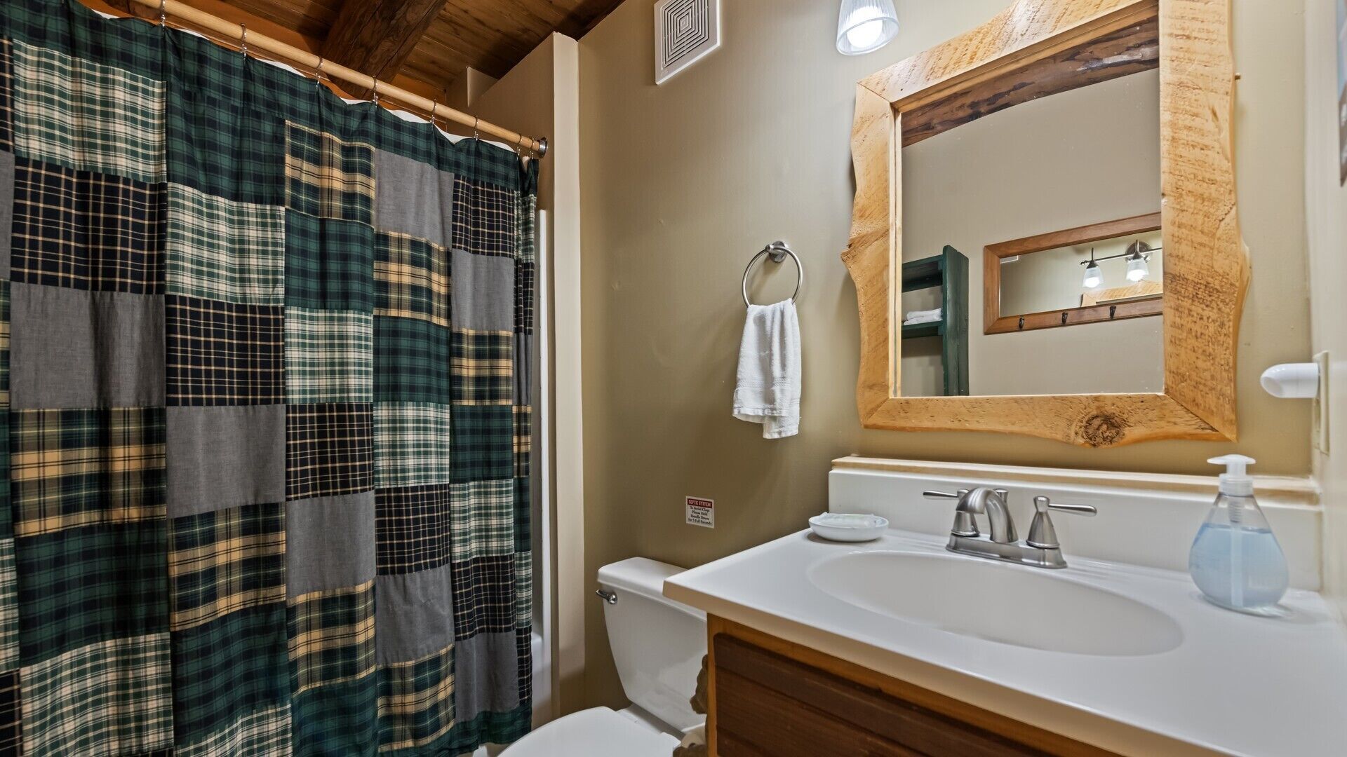A bathroom with a patchwork shower curtain, a wooden vanity, a sink with a soap dispenser, and a mirror with a wooden frame.