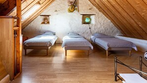 Ein gemütliches Schlafzimmer im Dachgeschoss mit drei Einzelbetten, Holzbalken und einem Globus an der Wand.