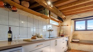 Eine Küche mit weißen Schränken, einer Holzausziehtafel, einer Weinflasche und einem Fenster.