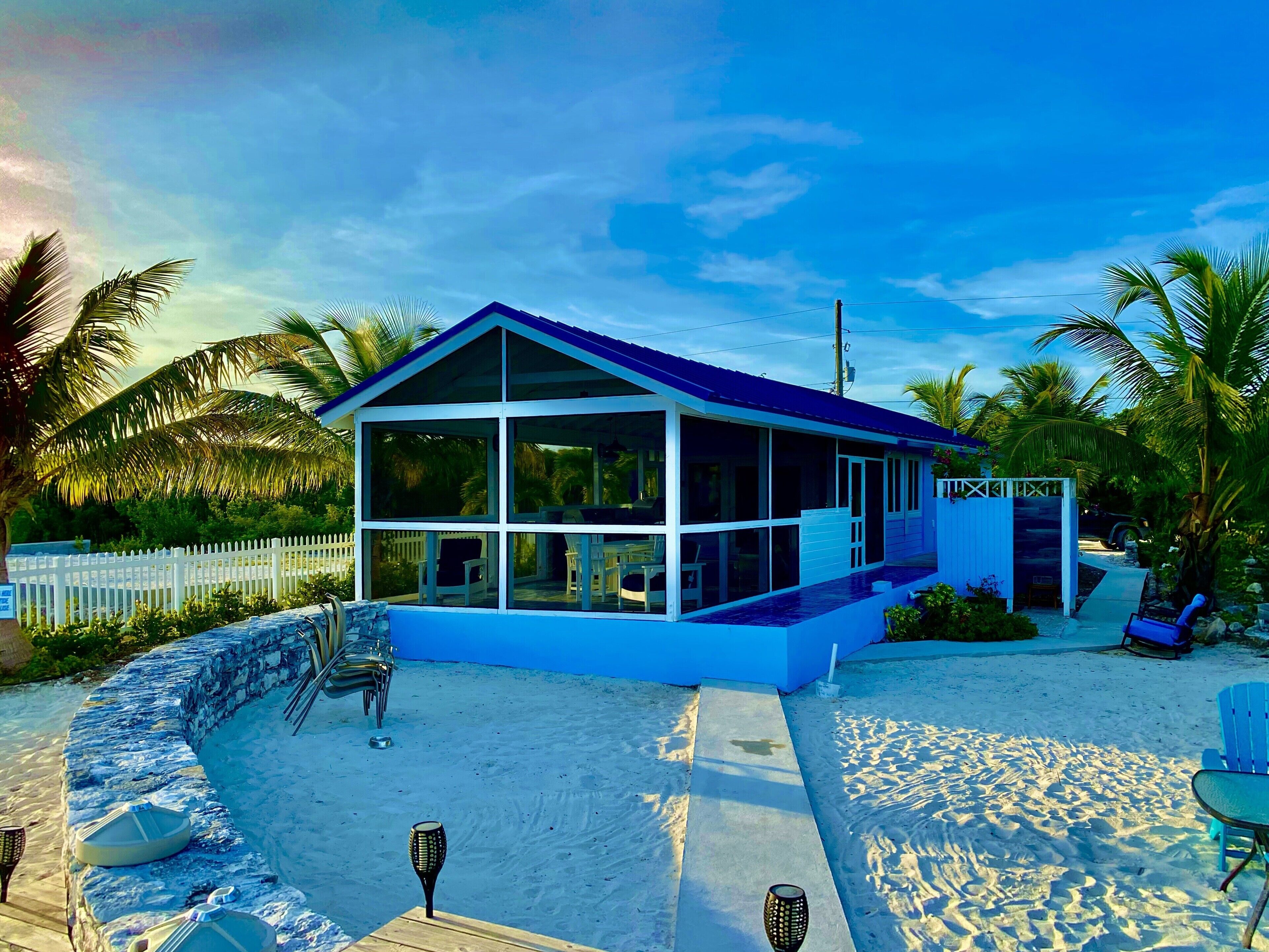 Una casa moderna frente a la playa, con un porche acristalado, piscina y cerca de piquetes blancos.