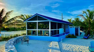 Una casa moderna frente a la playa, con un porche acristalado, piscina y cerca de piquetes blancos.