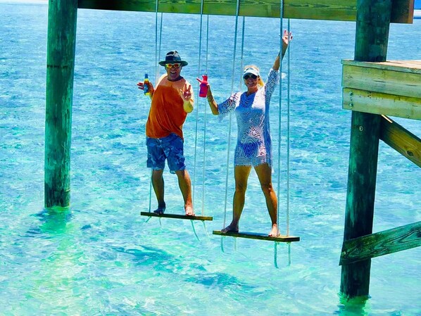 Two people on a wooden swing bridge over clear blue water.