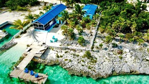 A resort with a dock, clear turquoise water, and a building with a blue roof. - Amazing Beachfront home the calm side of the island. Swimming & kayaking (Exuma)