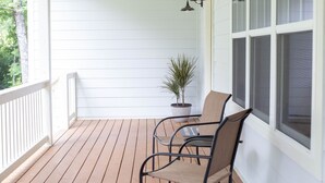 Eine Holzterrasse mit zwei Stühlen und einem Blumentopf, Wände mit weißer Holzverkleidung und ein Fenster mit Insektenschutzgitter.
