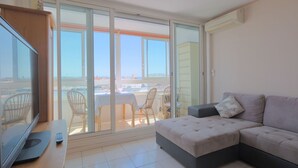 Ein modernes Wohnzimmer mit einem grauen Ecksofa, einem Flachbildfernseher und einem Balkon mit Korbstühlen und einem Tisch.