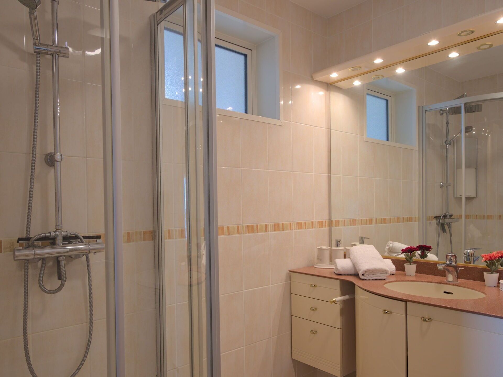 Un baño moderno con ducha envuelta en vidrio, tocador con lavamanos y espejo.
