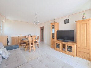 Una sala de estar moderna con sofá, mesa de comedor, sillas, televisor y armarios de madera.