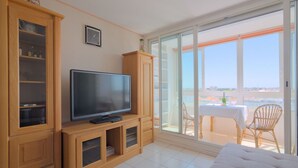 Ein modernes Wohnzimmer mit Flachbildfernseher, Holzschränken, einem Essbereich mit Tisch und Stühlen sowie einem Balkon mit Blick.