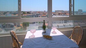 Ein Tisch mit einer Flasche, Gläsern und einem Teller mit Essen, mit Blick auf eine Stadt durch große Fenster.