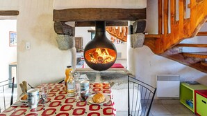 Un interior rústico con chimenea de piedra, vigas de madera y una mesa de comedor con mantel estampado.