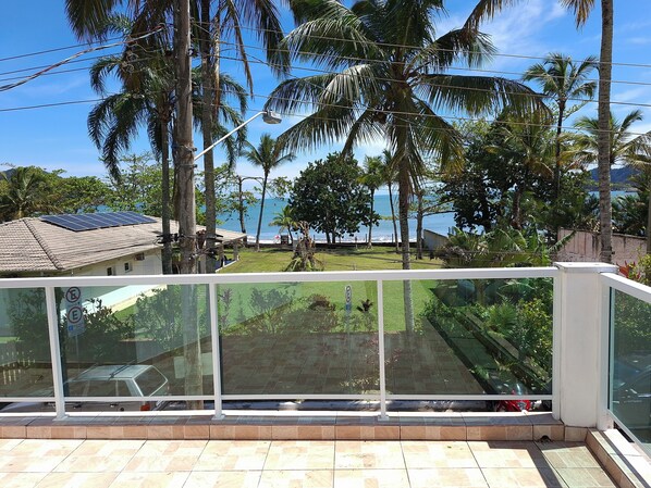 A balcony with a glass railing overlooking a coastal area with palm trees and a view of the sea.