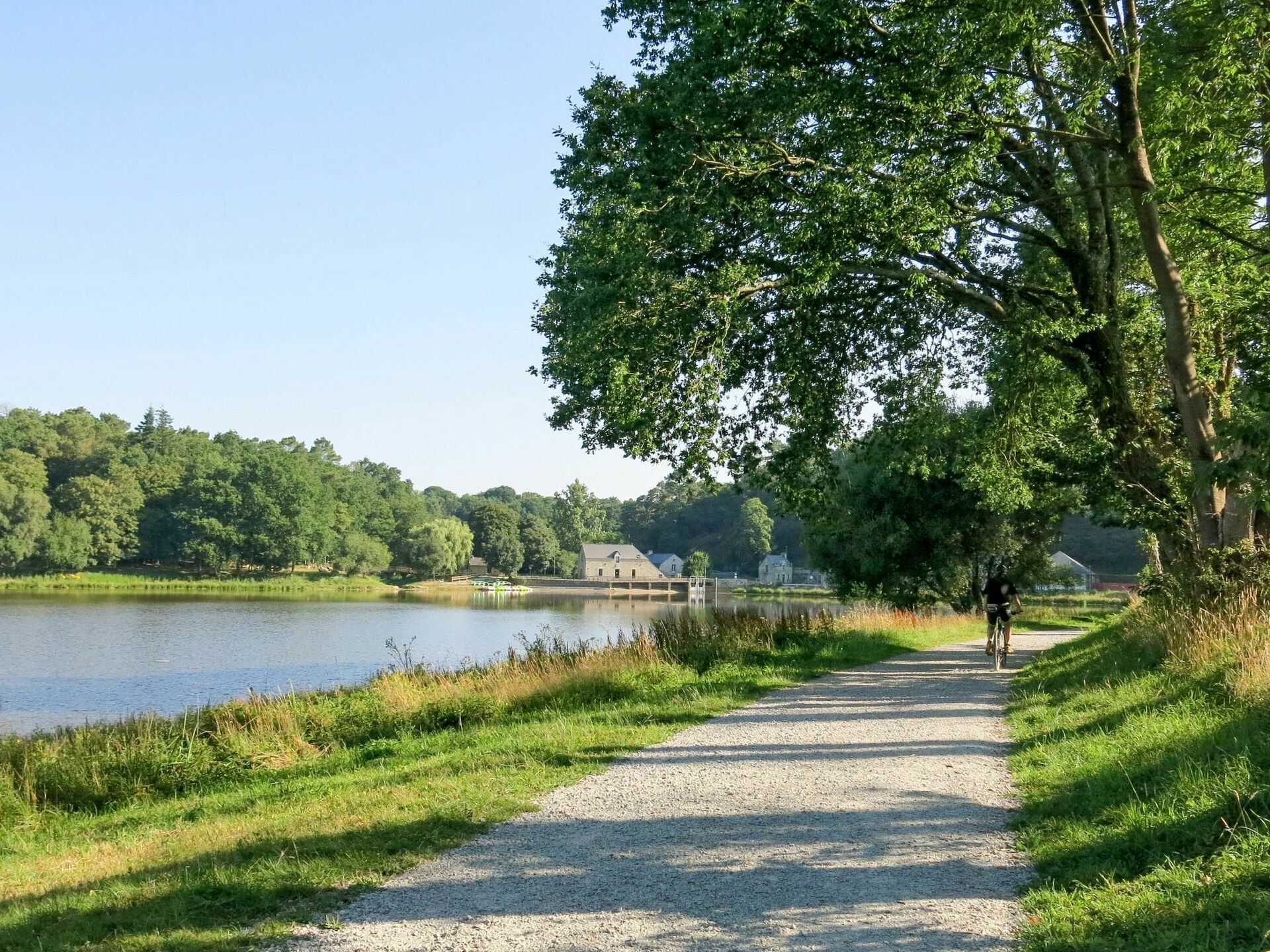 A gravel path beside a lake with a house in the background.
