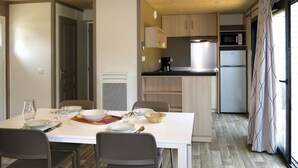 A compact kitchen with a dining area, featuring a white table set for four, a microwave, a refrigerator, and a coffee maker. - Nice apartment in villa for 6 people with WIFI, pool, TV, terrace and pets allowed (Rochefort-en-terre)