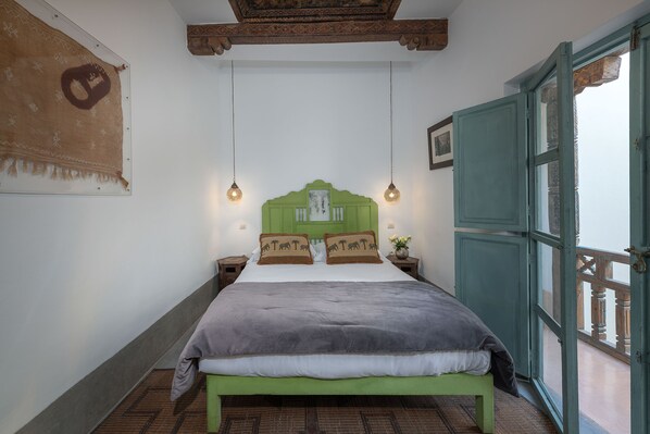 A room with a bed, a green headboard, two bedside tables, a hanging light fixture, and a window with a view.