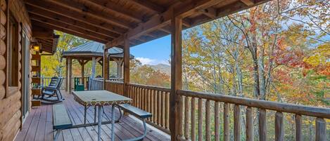 Una terraza de madera con una mesa y sillas, con vistas a un bosque con follaje otoñal.