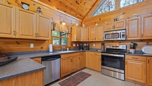 A kitchen with wooden cabinets, stainless steel appliances, a window with curtains, and a clock on the wall. - Mountaintop Getaway with Gazeebo Deck Hot Tub & Fireplace! Long range views! (Bryson City)