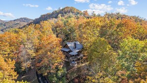 A cabin with a wrap-around porch, surrounded by autumn foliage and a mountain backdrop. - Mountaintop Getaway with Gazeebo Deck Hot Tub & Fireplace! Long range views! (Bryson City)