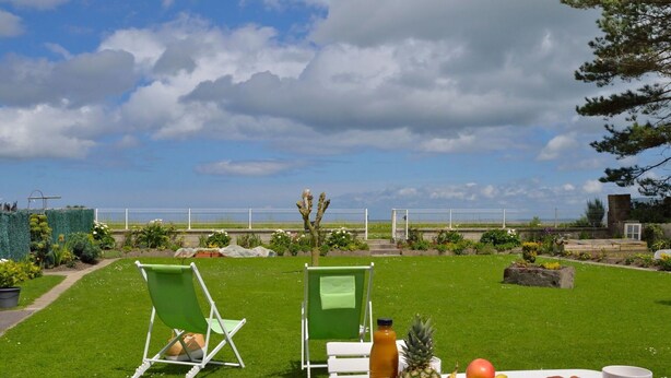 Ein Tisch im Freien mit Blick auf das Meer, eine Rasenfläche und ein weißer Zaun.