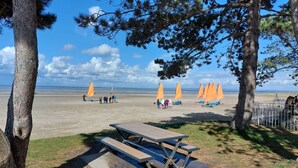 Ein Strand mit Picknicktischen und orangefarbenen Sonnenschirmen.