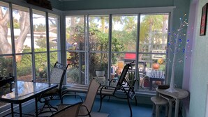 A sunroom with large windows, a table, chairs, and a small table with stools. - Quiet cozy home near Anna Maria Island, Robinson Preserve, DeSoto Nt’l Monument (Bradenton)
