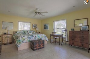 Une chambre à coucher avec un lit, une commode, un bureau, une chaise et une valise.