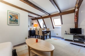 A room with a wooden ceiling, a dining table, a TV stand, and a framed poster on the wall.