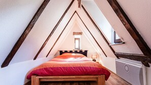 Un dormitorio acogedor en el ático con techo inclinado, una cama de madera, un tapete estampado y un radiador.