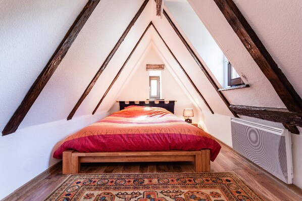 A cozy attic bedroom with a sloped ceiling, a wooden bed, a patterned rug, and a radiator.