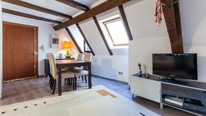 Un área de comedor con una mesa y sillas, un televisor sobre un mueble bajo, y una ventana con vistas.