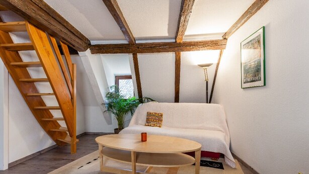 Una habitación acogedora con una escalera de madera, un sofá blanco, una mesa redonda y un cuadro enmarcado en la pared.