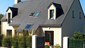 Uma casa de dois andares com telhado inclinado, vários claraboias e portão fechado.