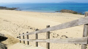 Uma praia arenosa com uma cerca de madeira e degraus que descem até a costa.