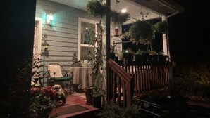 A porch with a wooden railing, potted plants, a table with chairs, and a statue. - Lovely 2 bedroom craftsman style home (Lincoln Beach)