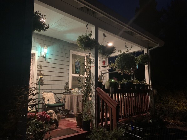 A porch with a wooden railing, potted plants, a table with chairs, and a statue.
