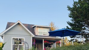 A house with a covered porch, a blue umbrella, and a well-maintained garden. - Lovely 2 bedroom craftsman style home (Lincoln Beach)