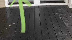 Una puerta principal con el número '15' sobre ella, un porche con piso de madera oscura y una cinta verde atada al picaporte.