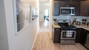 Una cocina con piso de madera, electrodomésticos de acero inoxidable y cuadros en la pared.