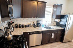 Una cocina con armarios de madera oscura, lavavajillas de acero inoxidable, cafetera y refrigerador.