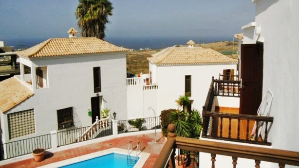 A residential area with white buildings, a swimming pool, and a view of the sea.