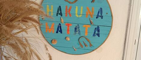A round sign with the text "HAKUNA MATATA" surrounded by seashells and a surfboard.