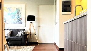En moderne stue med mørkt trægulv, en sort sofa med mønstrede puder, en gulvlampe og et indrammet abstrakt billede på væggen.